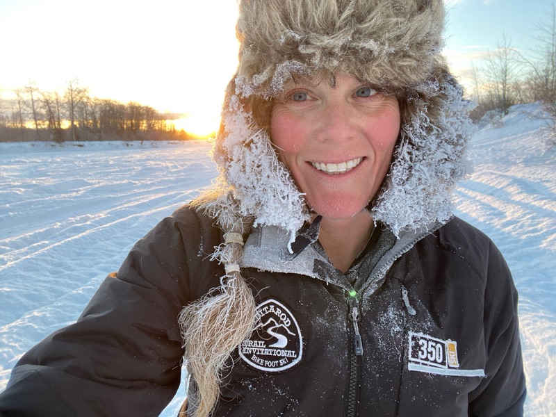 Sunny Stroeer smiling in a frost-rimmed fur hat at dawn on the Iditarod Trail