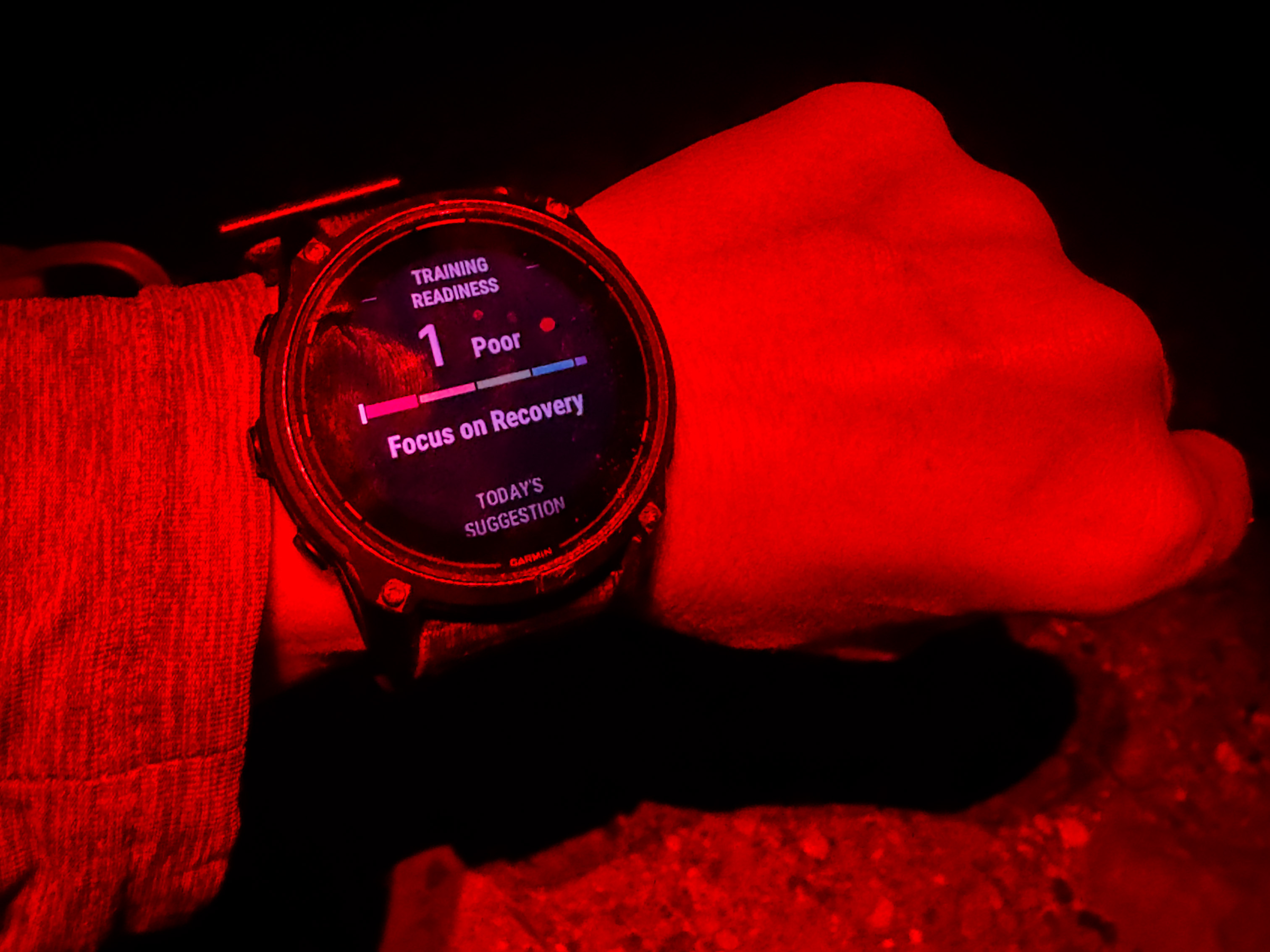 A Garmin watch illuminated by red headlamp shows Training Readiness 1 — Poor, Focus on Recovery