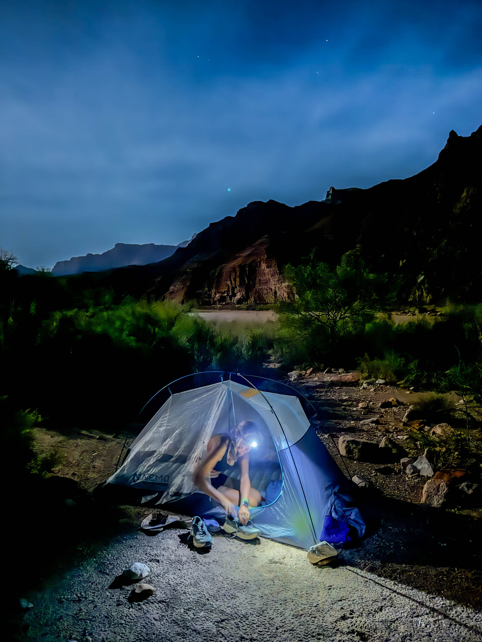 Mina Guli by headlamp inside a tent on the Grand Canyon floor at midnight, lacing up shoes for the pre-dawn push — the miles have to happen before sunrise in peak summer