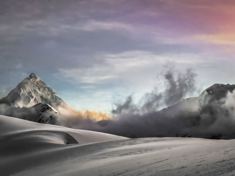 Snowbound peak emerging from clouds at first light
