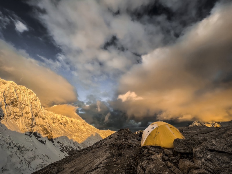 Yellow tent at high camp below sunlit glaciated walls