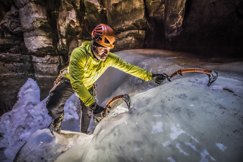 Ice climber on frozen flows inside a dark canyon