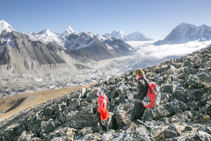 Two trekkers descending rocky moraine above a Himalayan glacier valley