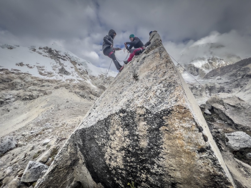 Climbers rigging ropes on a glacier-polished boulder