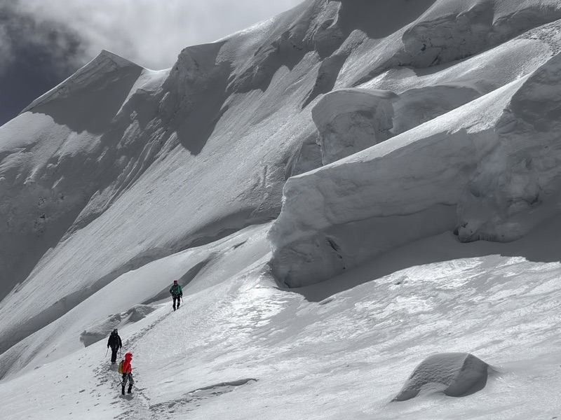 Three climbers crossing a snowfield beneath seracs