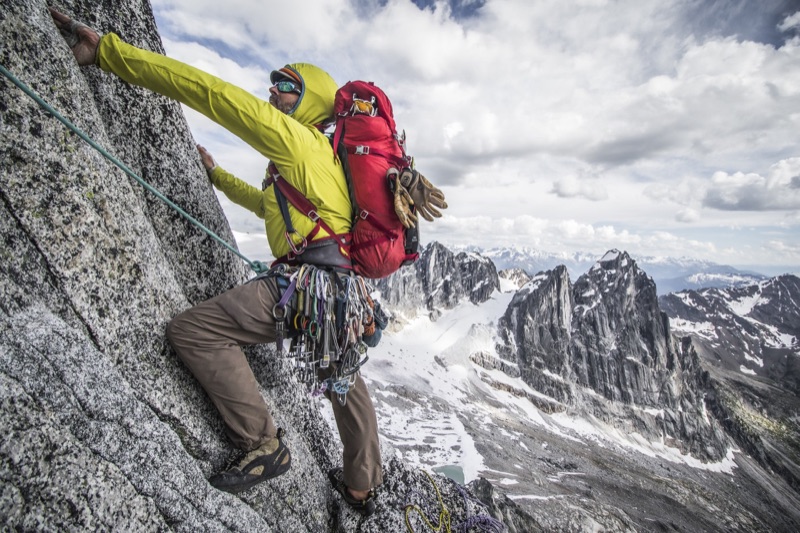 Climber with a full trad rack on steep granite above a glacial valley