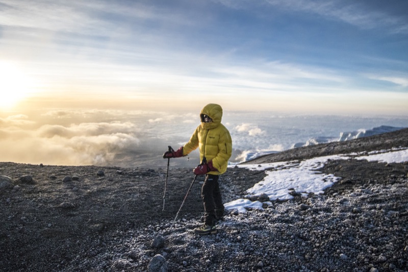 Mountaineer in a yellow down jacket above a sea of clouds at sunrise, glacier behind