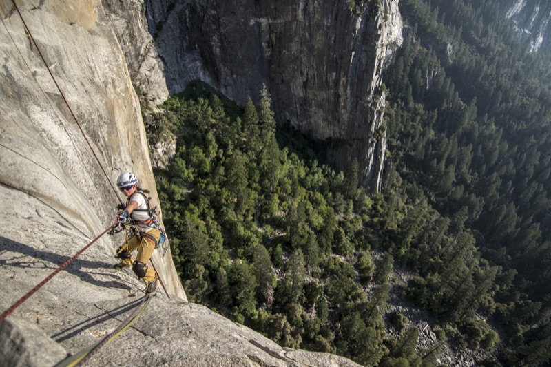 Climber on a fixed line high on a big wall above the forested valley floor
