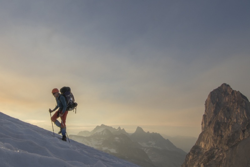 Mountaineer ascending a snow slope at sunset, rock tower behind