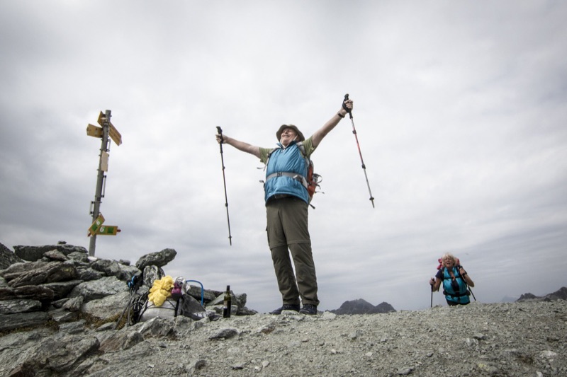 Hiker raising trekking poles beside summit signposts