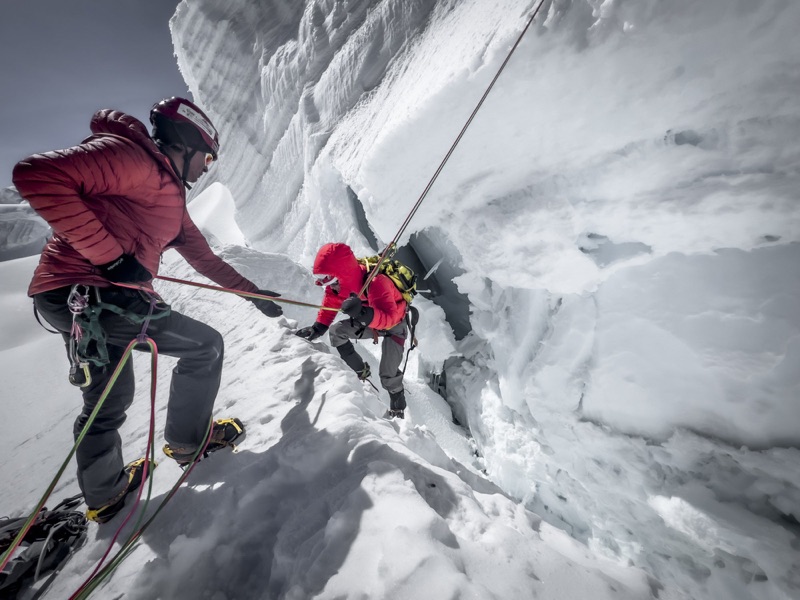 Roped climbers working a snow ledge beneath an ice cliff