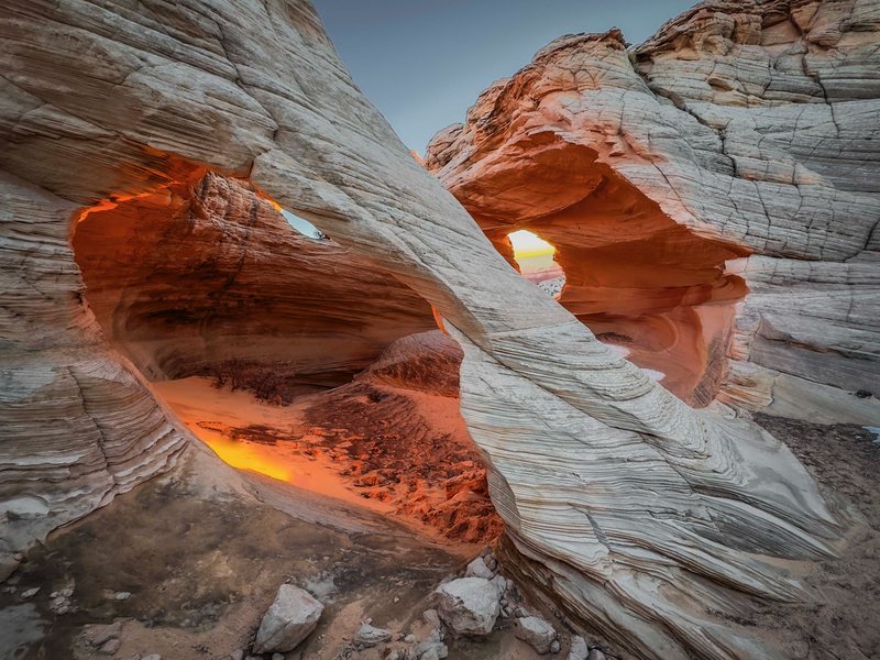 Two window-like openings in swirled white-and-orange sandstone glow with warm light at dusk