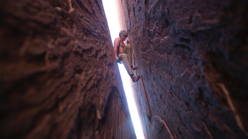 A climber stems between the narrow walls of a slot canyon with light glowing up from below